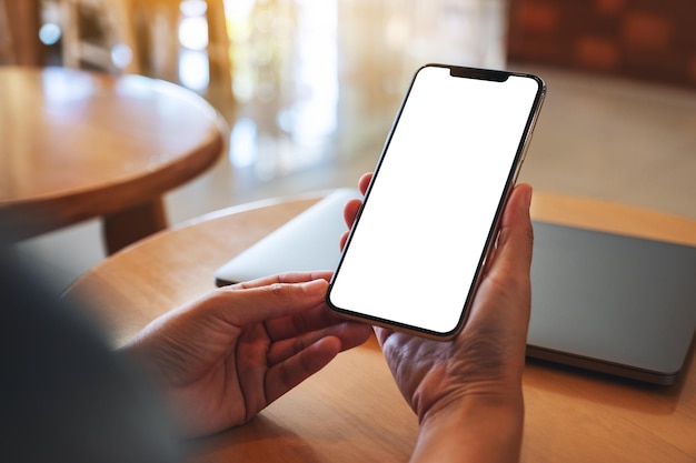 Immagine del modello di una donna che tiene il telefono cellulare con lo schermo del desktop bianco vuoto con il laptop sul tavolo