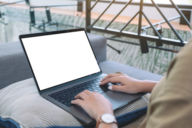 Immagine del modello di una donna che utilizza e digita sulla tastiera del laptop con schermo bianco vuoto mentre è seduto in salotto