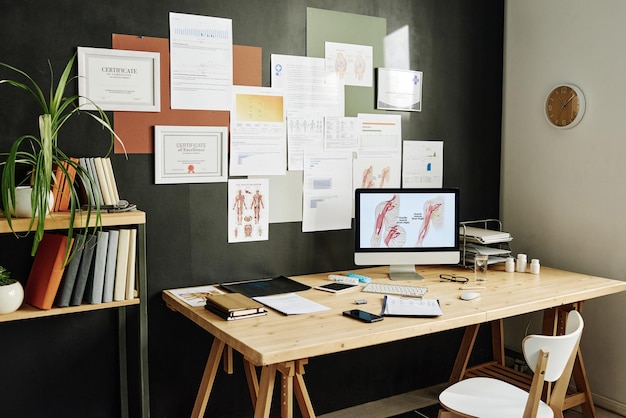 Immagine del moderno posto di lavoro del medico con monitor di computer e certificati sul muro