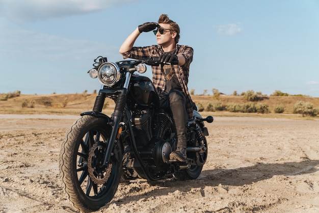 Immagine del motociclista serio concentrato del giovane sulla bici all'aperto al campo del deserto.