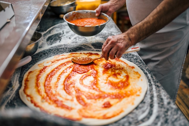 Immagine del primo piano del cuoco unico che produce pizza.