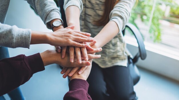 Immagine del primo piano del team aziendale in piedi e unendo le mani insieme in ufficio