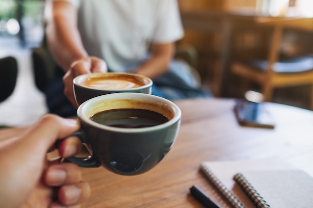 Immagine del primo piano dell'uomo e della donna che tintinnano tazze da caffè bianche nella caffetteria