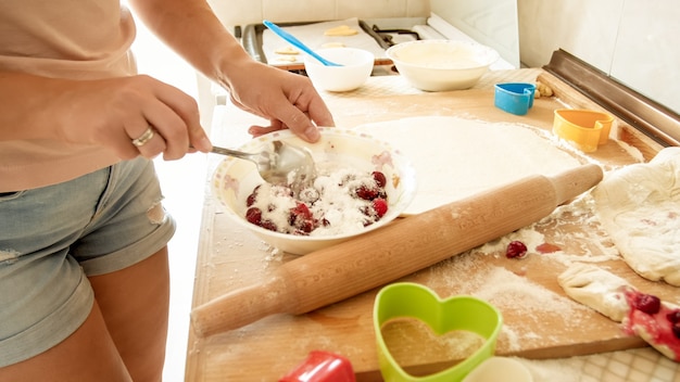 Immagine del primo piano della giovane casalinga che versa lo zucchero in una grande ciotola con bacche fresche mentre prepara la salsa per la torta