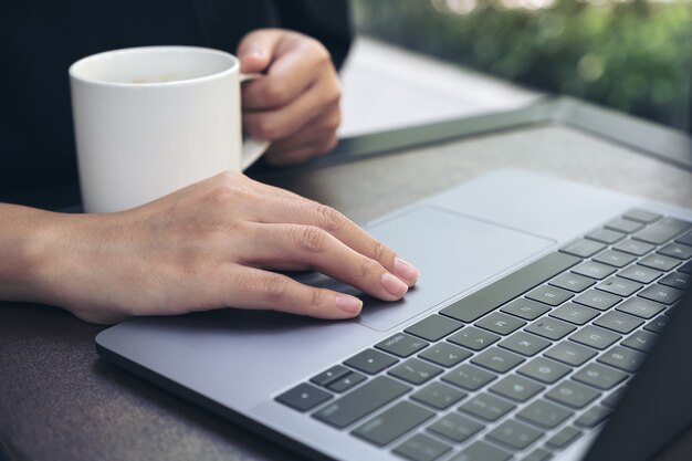 Immagine del primo piano della mano che lavora e che scrive sulla tastiera del computer portatile mentre bevendo caffè