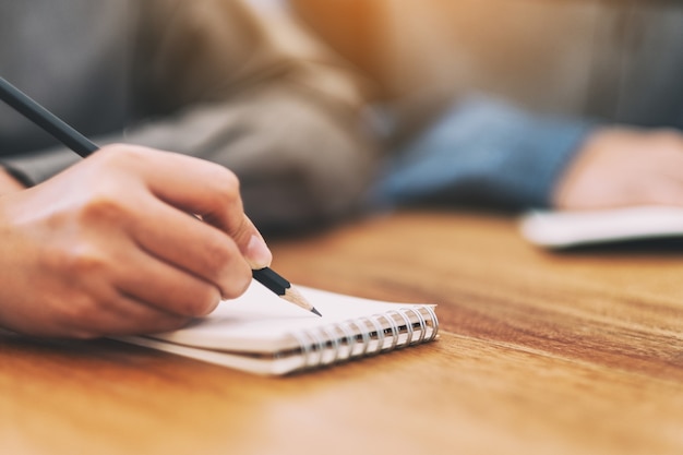 Immagine del primo piano della mano di una donna che scrive su un taccuino bianco su un tavolo di legno