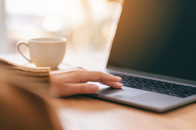 Immagine del primo piano della mano di una donna che usa e tocca il touchpad del laptop su un tavolo di legno