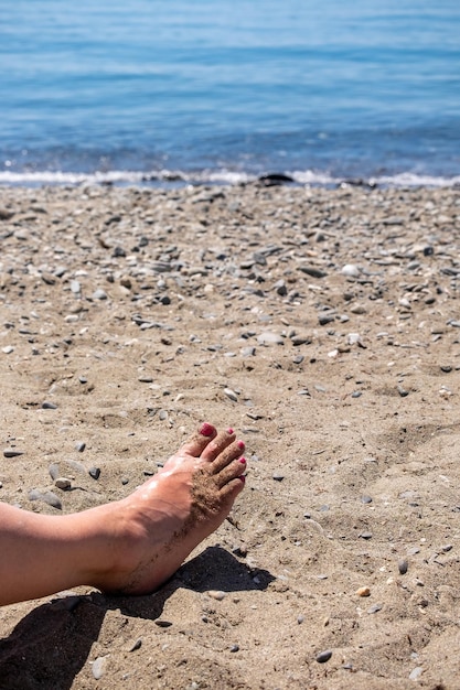 Immagine del primo piano delle gambe della donna senior che si siede rilassata sulla spiaggia sabbiosa