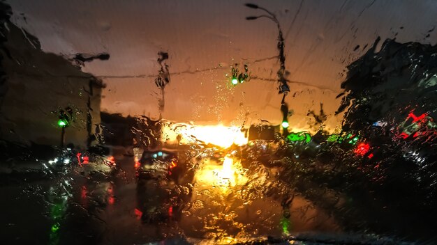 Immagine del primo piano delle goccioline sul parabrezza bagnato dell'auto sotto la pioggia alla luce del tramonto. Colpo astratto di parabrezza bagnato e raggi di sole