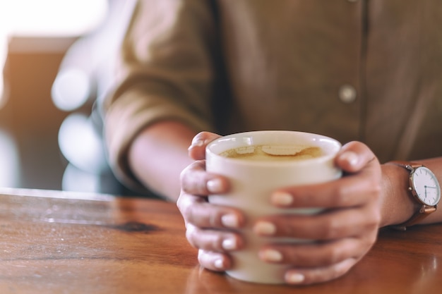 Immagine del primo piano delle mani della donna che tengono una tazza di caffè caldo sulla tavola di legno