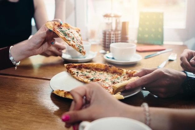 Immagine del primo piano di amici che condividono la tradizionale pizza italiana e bevono tè in un bar