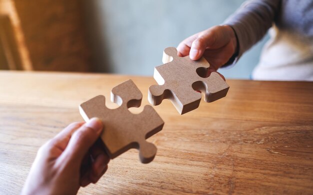 Immagine del primo piano di due persone che tengono e mettono insieme un pezzo di puzzle di legno