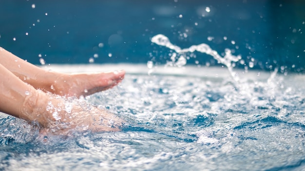 Immagine del primo piano di gambe e calci a piedi nudi e spruzzi d'acqua in piscina