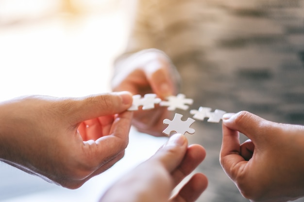 Immagine del primo piano di molte persone che tengono e mettono insieme un pezzo di puzzle bianco