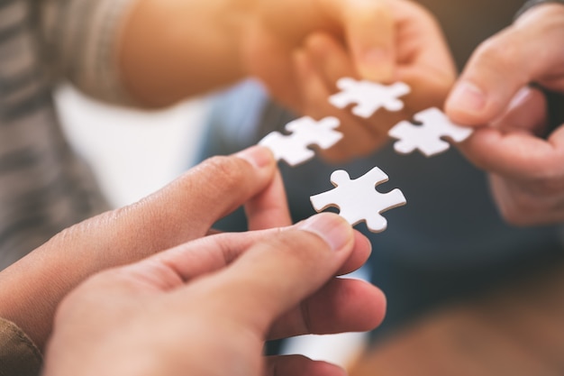 Immagine del primo piano di molte persone che tengono e mettono insieme un pezzo di puzzle bianco