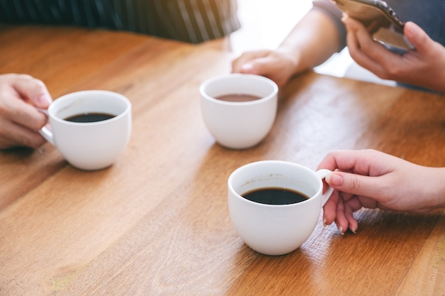 Immagine del primo piano di tre persone che tengono tazze di caffè da bere su un tavolo di legno