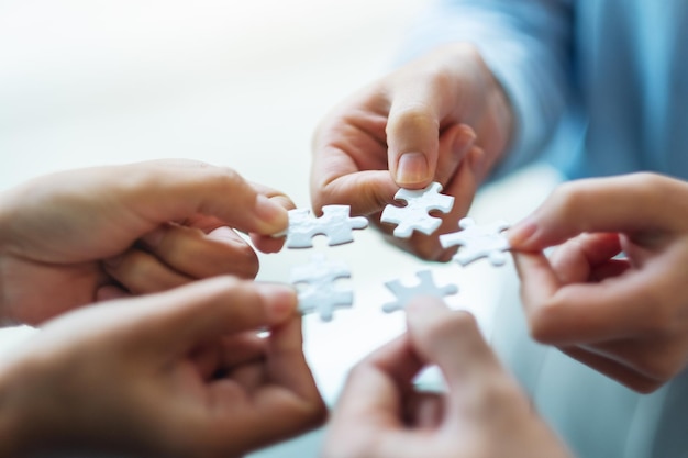 Immagine del primo piano di un gruppo di persone che tengono e che mettono insieme un pezzo di puzzle bianco