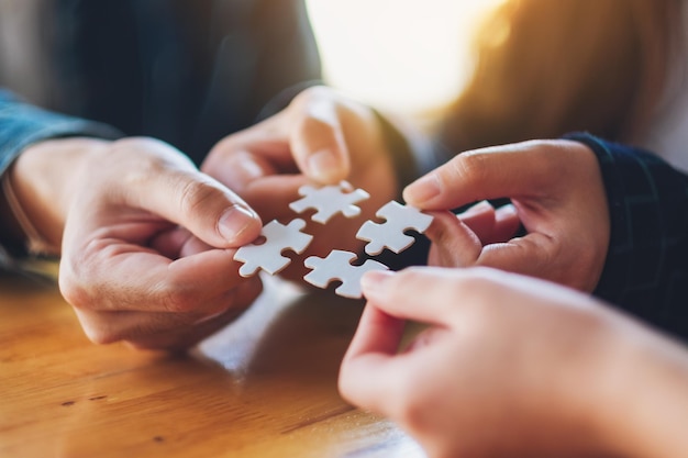 Immagine del primo piano di un gruppo di persone che tengono e mettono insieme un pezzo di puzzle bianco