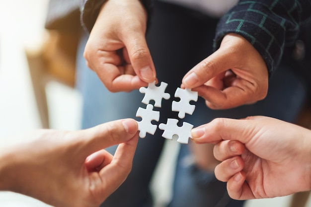 Immagine del primo piano di un gruppo di persone che tengono e mettono insieme un pezzo di puzzle bianco