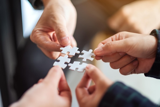 Immagine del primo piano di un gruppo di persone che tengono e mettono insieme un pezzo di puzzle bianco