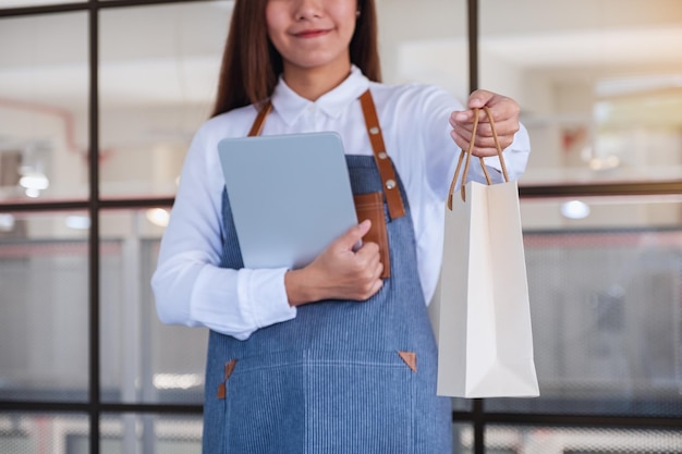 Immagine del primo piano di un'imprenditrice che tiene in mano una tavoletta digitale mentre dà la borsa della spesa al cliente