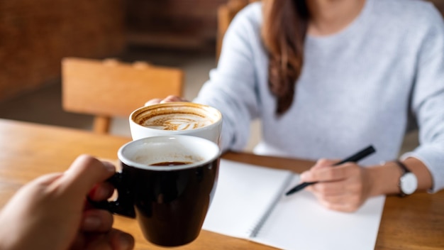 Immagine del primo piano di un paio di persone che tintinnano le tazze di caffè mentre lavorano insieme