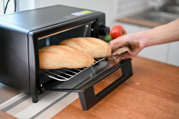 Immagine del primo piano di un uomo che mette la baguette nel forno che cuoce la pasta o riscalda il pane nel forno