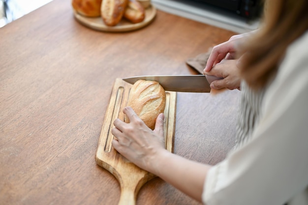 Immagine del primo piano di una bella coppia che taglia il pane con il coltello insieme preparando il cibo in cucina