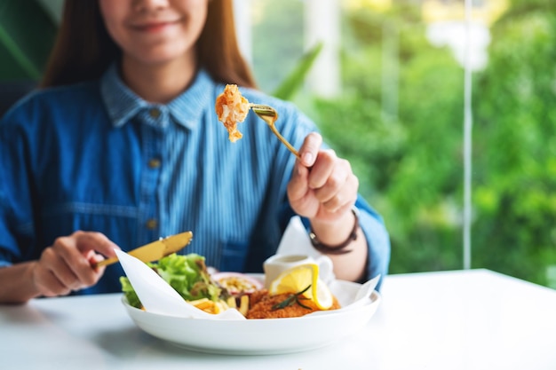 Immagine del primo piano di una bella donna asiatica che mangia pesce e patatine fritte sul tavolo del ristorante