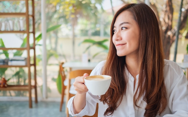 Immagine del primo piano di una bella donna asiatica che tiene e beve caffè caldo sentendosi bene al bar