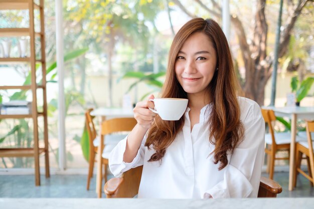 Immagine del primo piano di una bella donna asiatica che tiene e beve caffè caldo sentendosi bene al bar