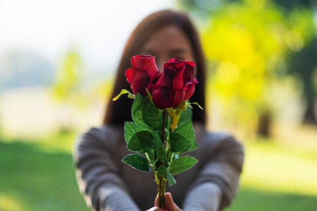 Immagine del primo piano di una bella donna asiatica che tiene e che dà fiori di rose rosse nel parco