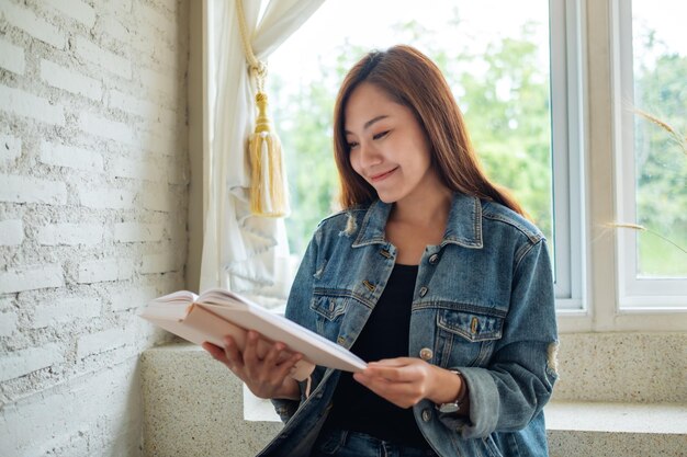 Immagine del primo piano di una bella donna asiatica seduta e che legge un libro a casa