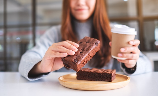 Immagine del primo piano di una bella donna che tiene e mangia un pezzo di torta brownie mentre beve caffè