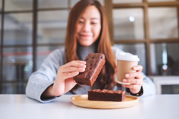 Immagine del primo piano di una bella donna che tiene e mangia un pezzo di torta brownie mentre beve caffè