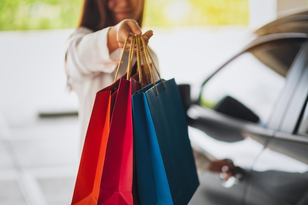 Immagine del primo piano di una bella donna che tiene e mostra le borse della spesa mentre apre la portiera della macchina nel parcheggio del centro commerciale