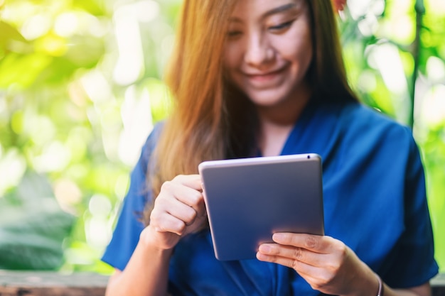 Immagine del primo piano di una bella donna che tiene e usa un tablet pc mentre è seduta in giardino