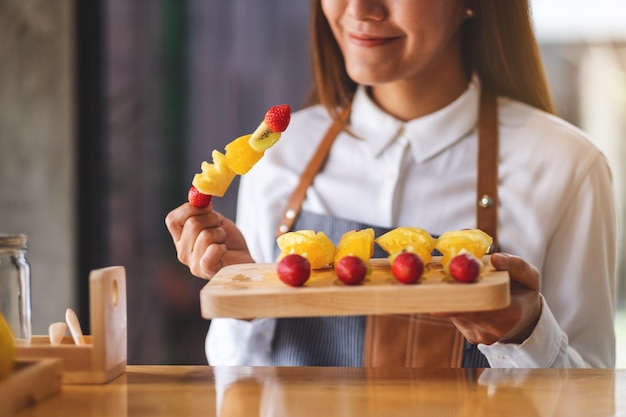 Immagine del primo piano di una bella donna chef che tiene frutta fresca mista su spiedini in un piatto di legno