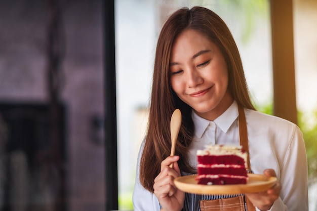 Immagine del primo piano di una bella donna chef femminile che cuoce e mangia un pezzo di torta di velluto rosso nel vassoio di legno