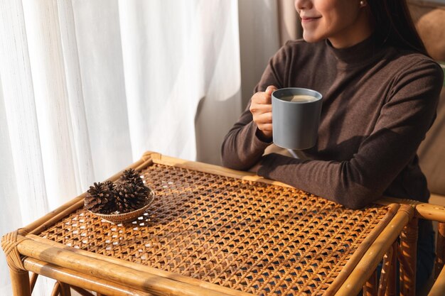 Immagine del primo piano di una bella giovane donna asiatica che beve caffè caldo a casa al mattino