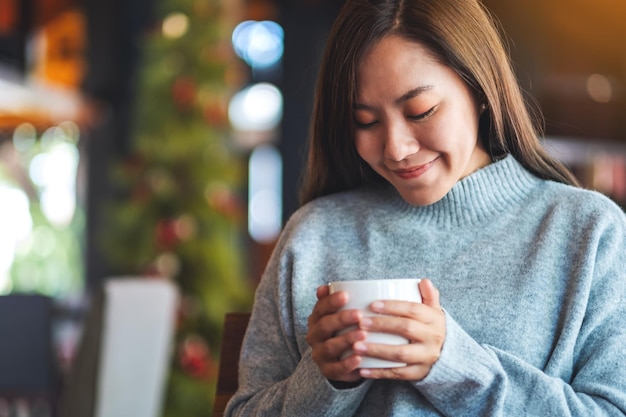 Immagine del primo piano di una bella giovane donna asiatica che tiene e beve caffè caldo nella caffetteria