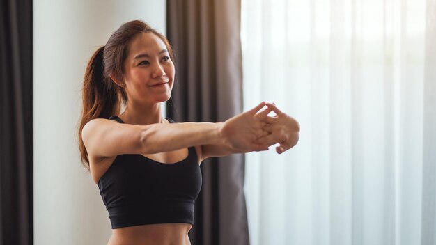 Immagine del primo piano di una bellissima giovane donna asiatica che allunga le braccia per riscaldarsi prima dell'allenamento a casa