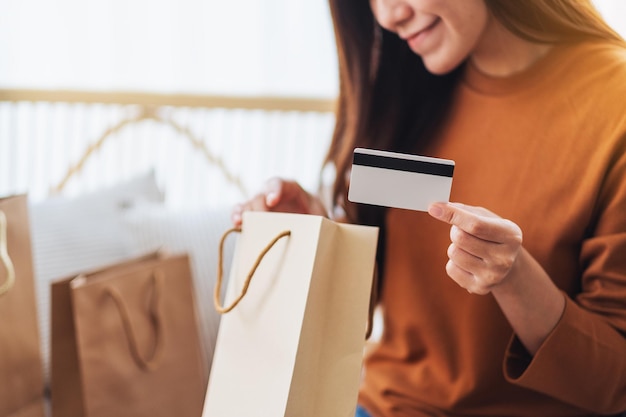 Immagine del primo piano di una bellissima giovane donna che tiene in mano una carta di credito mentre apre le borse della spesa a casa