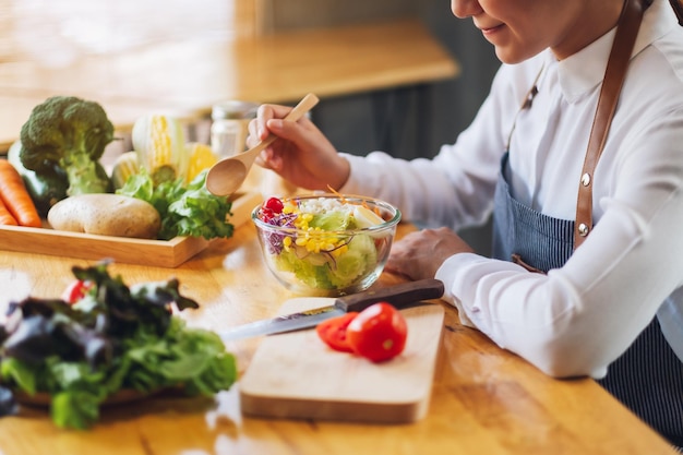 Immagine del primo piano di una chef donna che cucina e mangia una ciotola di insalata di verdure miste fresche in cucina