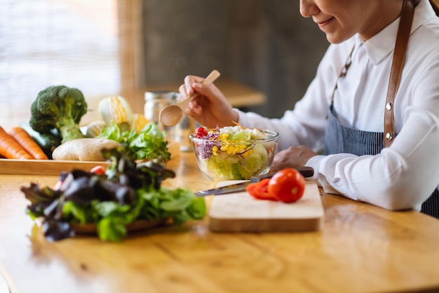 Immagine del primo piano di una cuoca che cucina e mangia insalata di verdure miste fresche in cucina