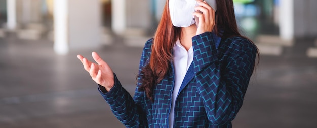 Immagine del primo piano di una donna asiatica che indossa una maschera protettiva, che usa e parla al telefono cellulare per il concetto di assistenza sanitaria e Covid-19