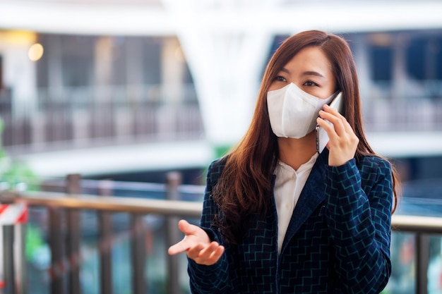 Immagine del primo piano di una donna asiatica che indossa una maschera protettiva, che usa e parla al telefono cellulare per il concetto di assistenza sanitaria e Covid-19
