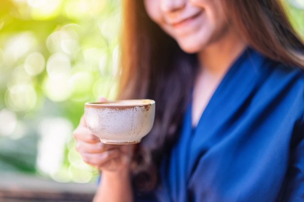 Immagine del primo piano di una donna asiatica che tiene e beve caffè caldo in giardino