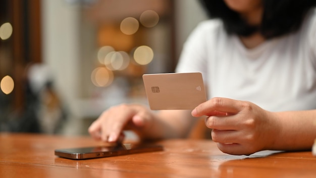 Immagine del primo piano di una donna asiatica in possesso di una carta di credito e utilizzando il suo smartphone