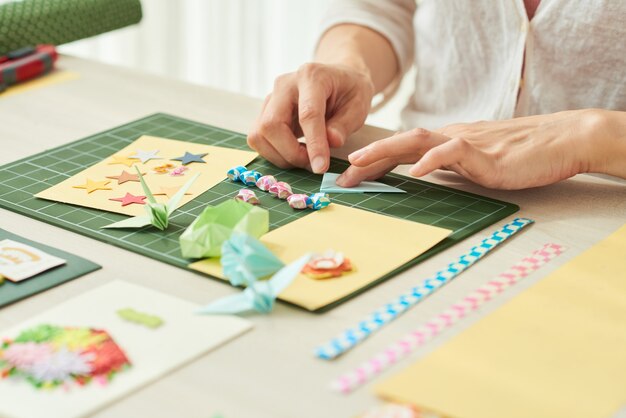 Immagine del primo piano di una donna che fa elementi come stelle, gru o fiori per biglietti di auguri con...